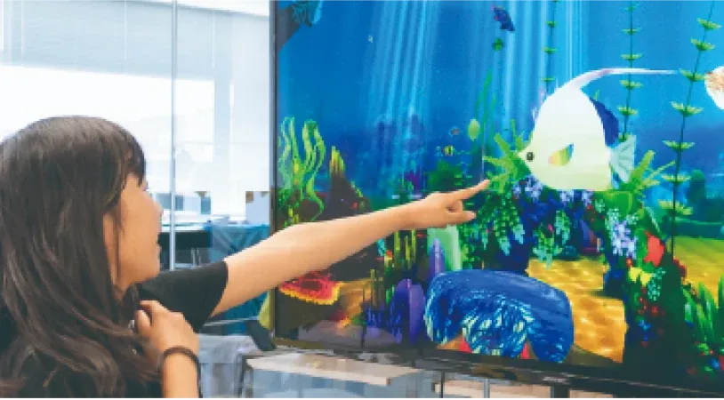 大画面に映るデジタル水族館を指さす子ども