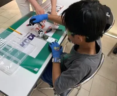 手袋をつけて、専用の工具でスマートフォンを分解する子ども