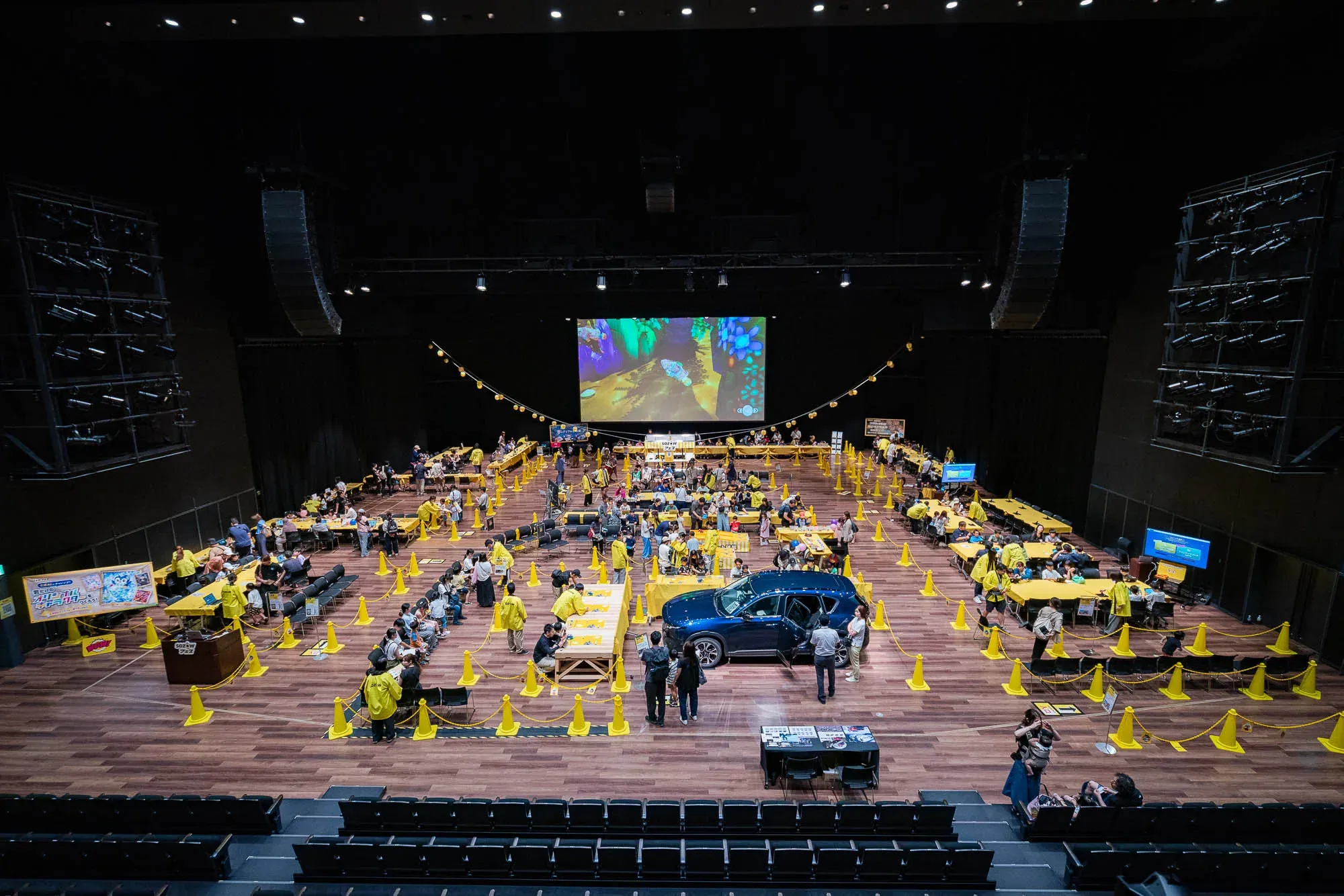 メインホールを客席の後方から見た全景。体験ブースのテーブルが並び、中央に展示車両が置かれている