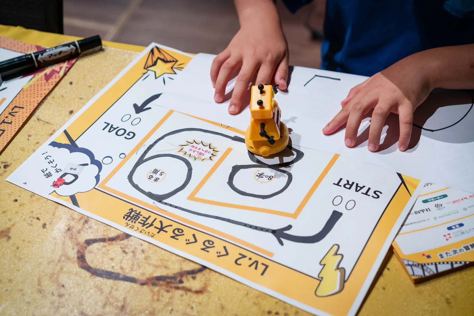 ロボットが走るコースを自分で描き込んだ用紙と、その上を走るロボット