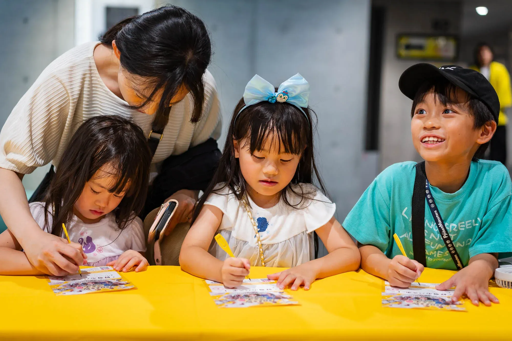 黄色いテーブルで、3人の子どもが並んで配布シートに書き込んでいる様子