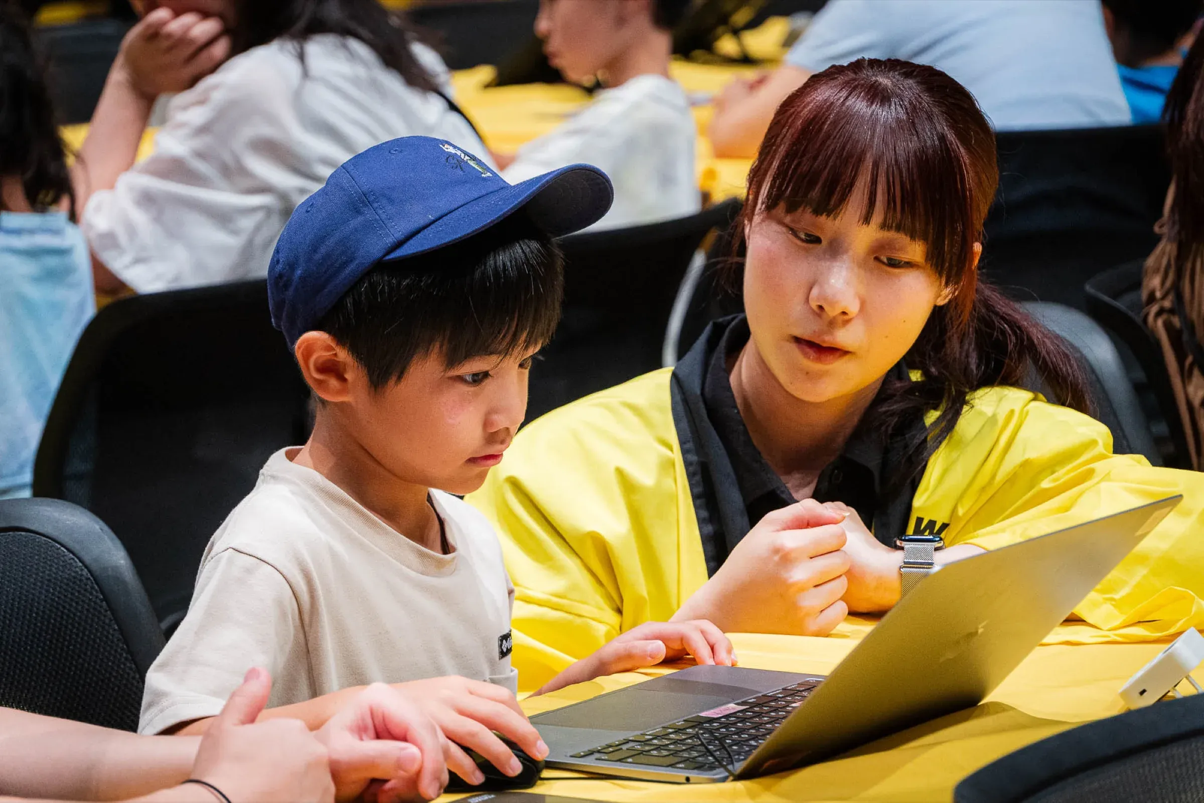 スタッフが子どもの隣でノートパソコンの操作を教えている様子