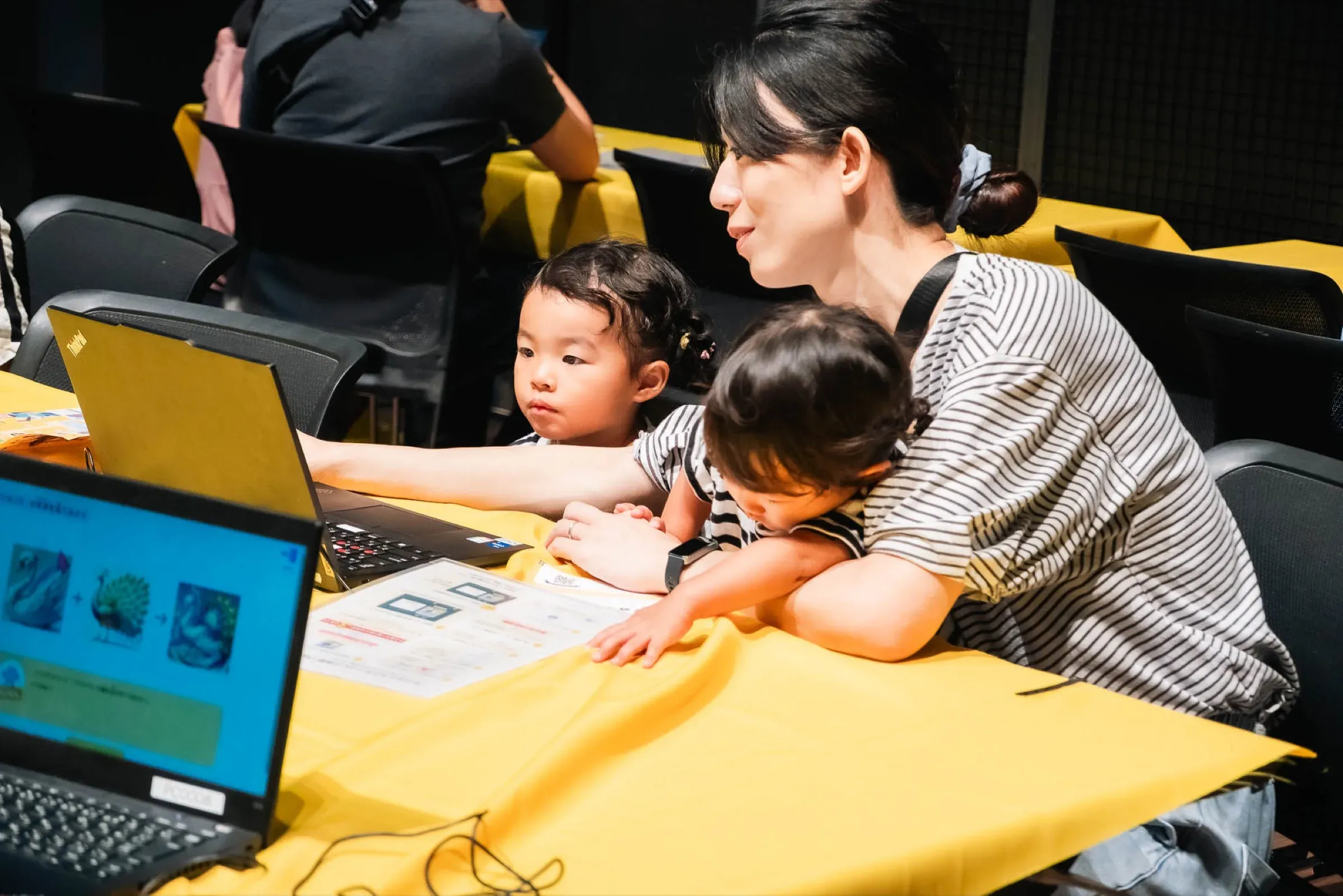 ブースのノートパソコンに集中する子どもたちと保護者