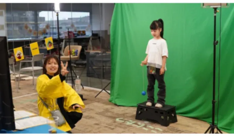 グリーンバックの前で撮影に挑戦する子どもと、進行するスタッフ